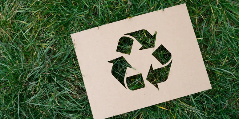 Recycling symbol cut from cardboard placed on grass.
