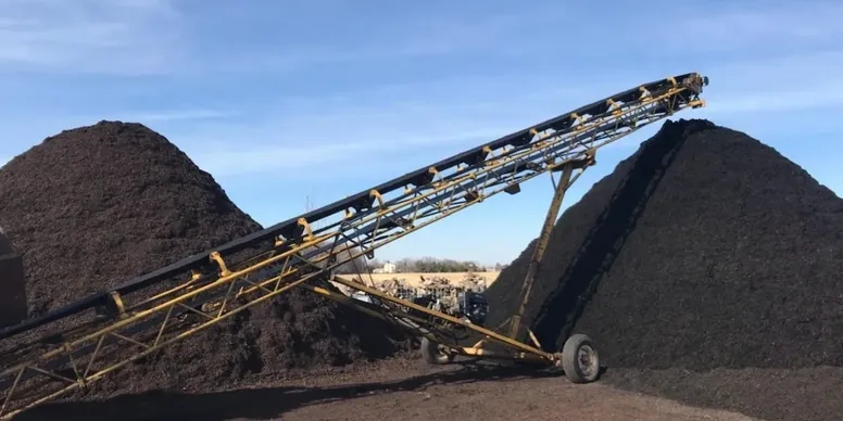 Industrial conveyor belt transporting soil or minerals outdoors.