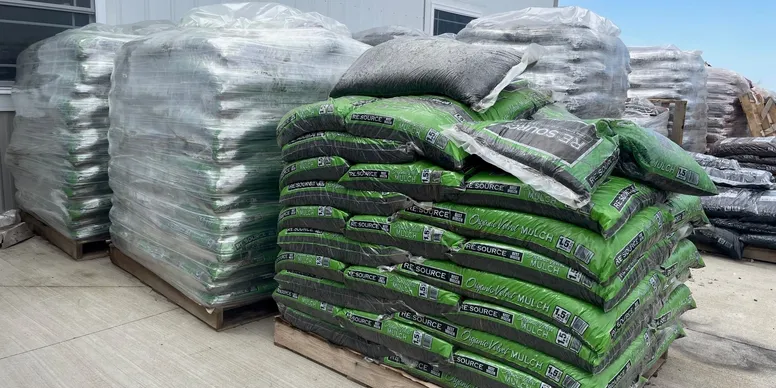 Stacks of green and white bags stored outdoors, covered partially by a tarp.