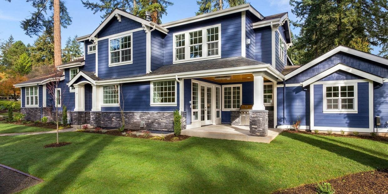 Modern two-story house with blue siding and stone accents on a green lawn.