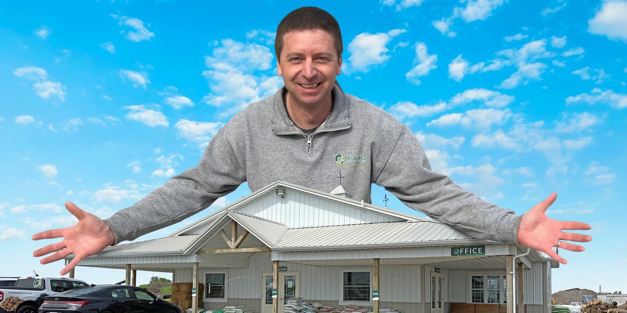 Man smiling behind a model house against a blue sky.