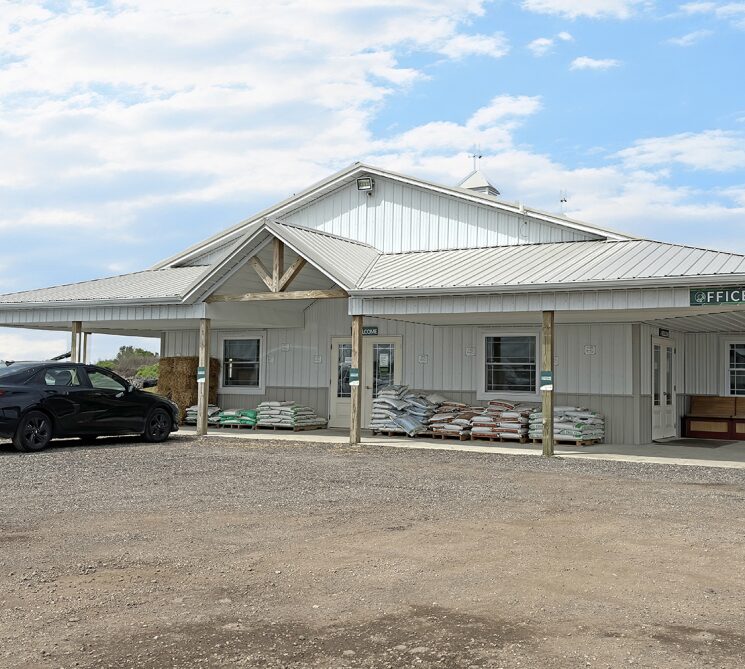 A modern white building with a metal roof and a gravel driveway under a cloudy sky.