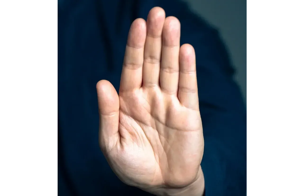 Close-up of a raised hand with fingers together against a dark background.