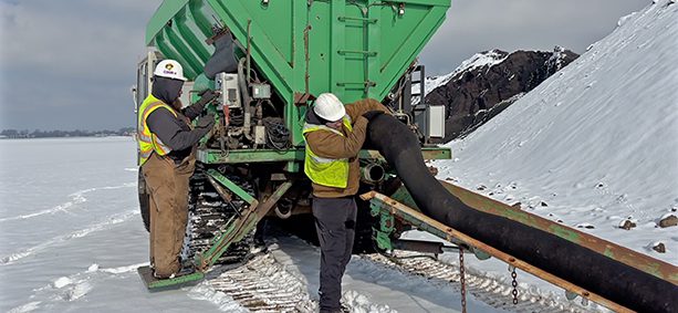 Workers operating equipment on snowy landscape.