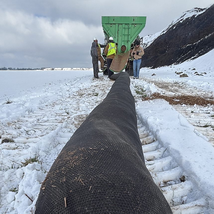 Workers installing erosion control on snowy field.