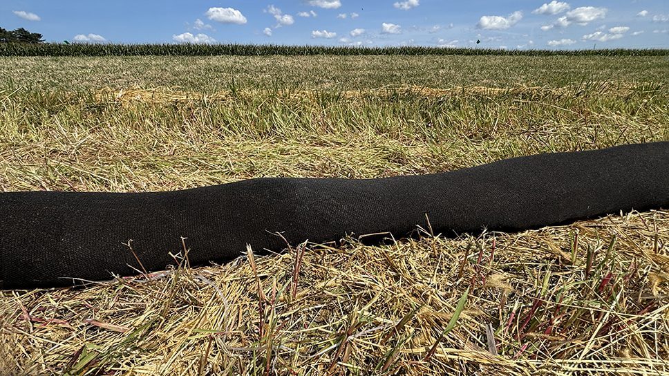 Black pipe on grassy field under blue sky.