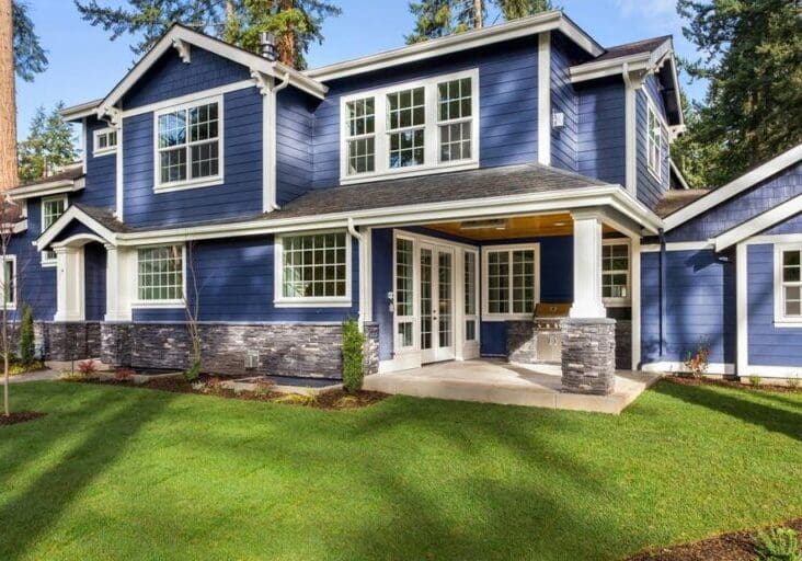 Modern two-story house with blue siding and stone accents on a green lawn.