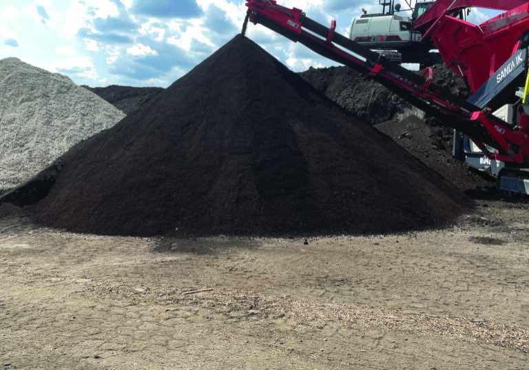 Red conveyor dumping dark mulch onto large pile